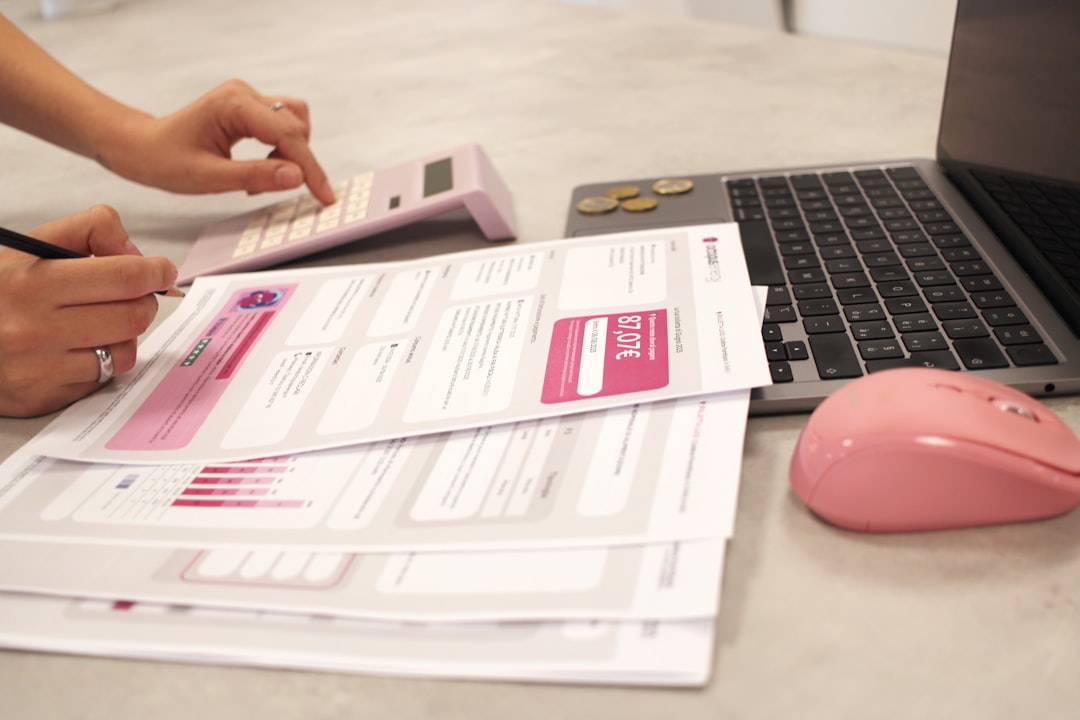 Hands working on financial documents and laptop
